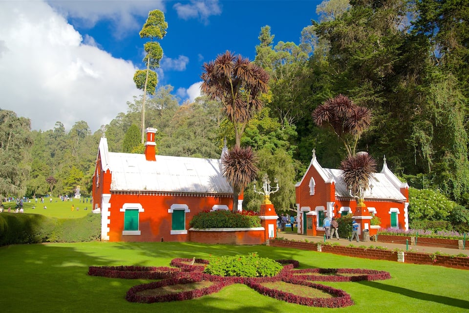 Un edificio de ladrillo rojo con puertas verdes y detalles blancos, rodeado de abundante vegetación y un jardín cuidado.