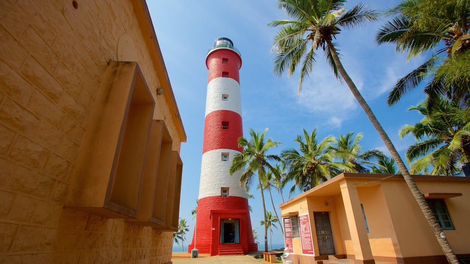 A red and white lighthouse, palm trees, and a building with a sign.