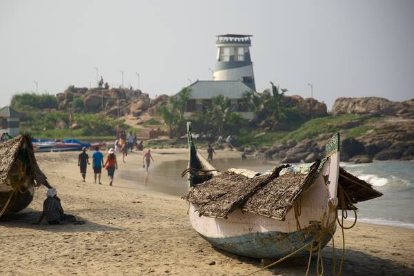 Ein Strand mit traditionellen Booten, einem Leuchtturm und Menschen, die spazieren gehen.