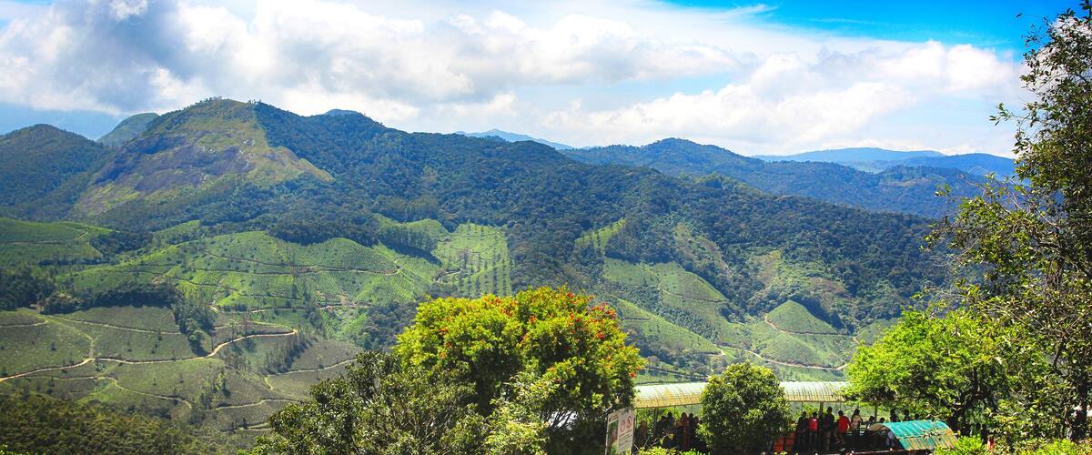 A mountainous landscape with terraced fields and a group of people gathered near a structure.