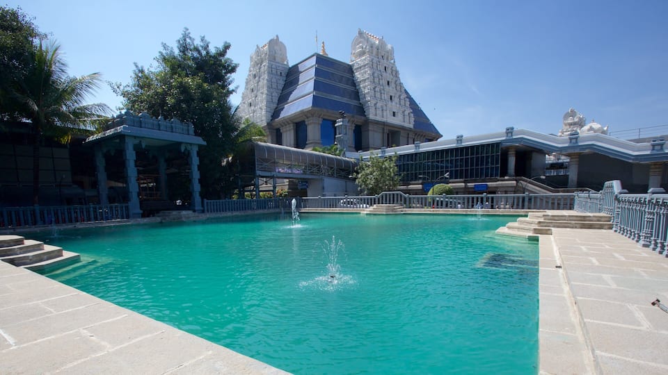 A swimming pool with a fountain, surrounded by a white fence and steps leading up to a temple-like structure with two towers.