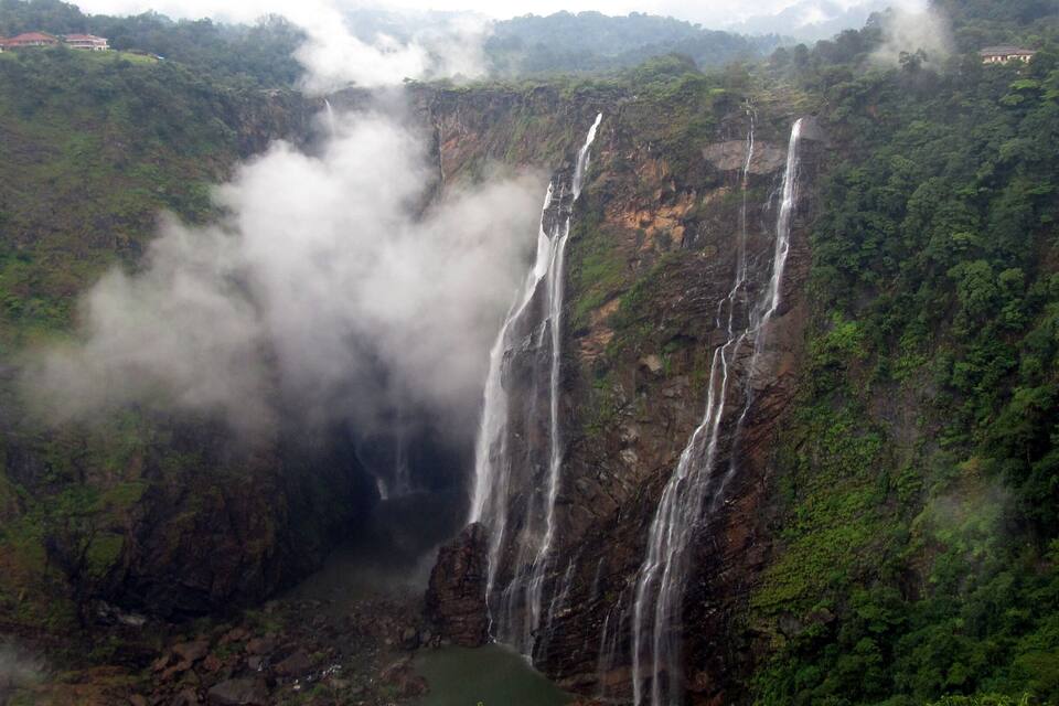 Ein mehrstufiger Wasserfall stürzt über eine steile, bewaldete Klippe.
