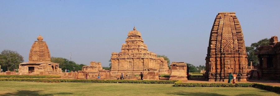 Ancient stone structures with intricate carvings, surrounded by well-maintained lawns and a clear sky.
