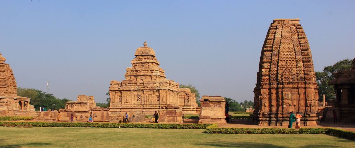 Ancient stone structures with intricate carvings, surrounded by well-maintained lawns and a clear sky.