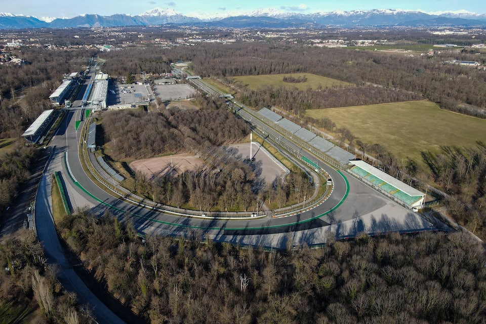 Vista aérea de uma pista de corrida, com uma floresta ao redor e montanhas distantes.