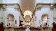 Interior de iglesia con techos abovedados, bancos de madera y un pasillo central que conduce al altar.