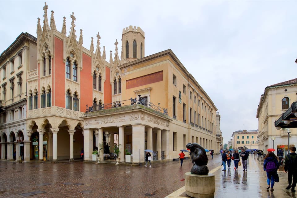 A historic building with ornate Gothic architecture, a statue, and a wet cobblestone square.
