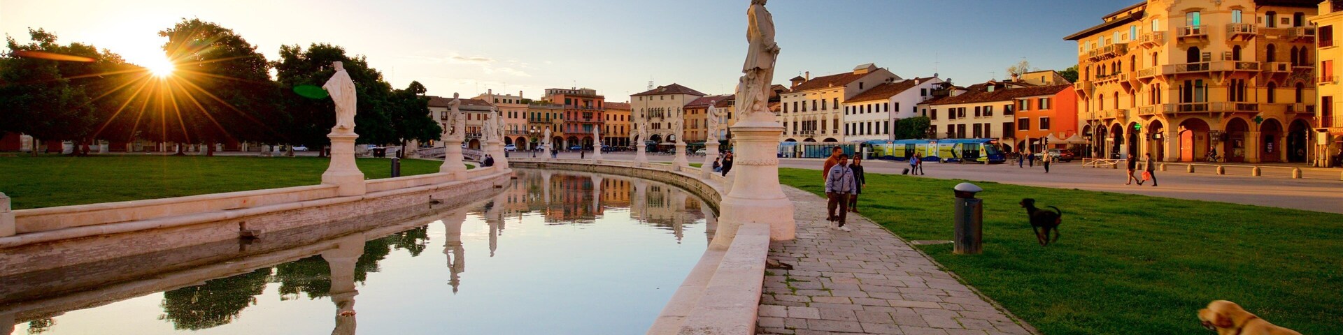 Uma fonte com estátuas, área gramada e edifícios históricos ao fundo.