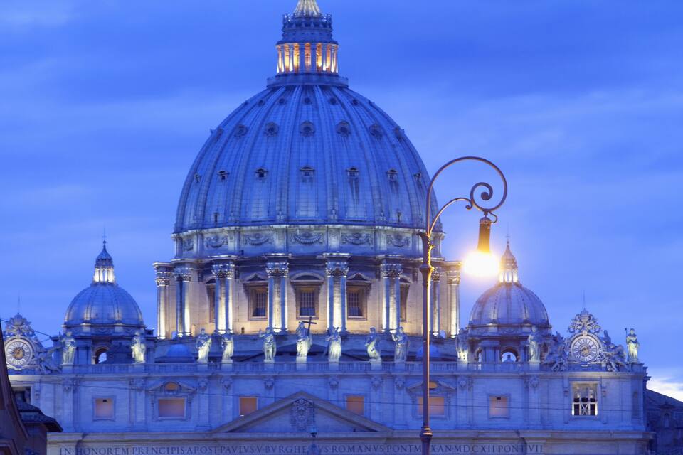 A grand building with a large dome and columns, illuminated by street lamps.