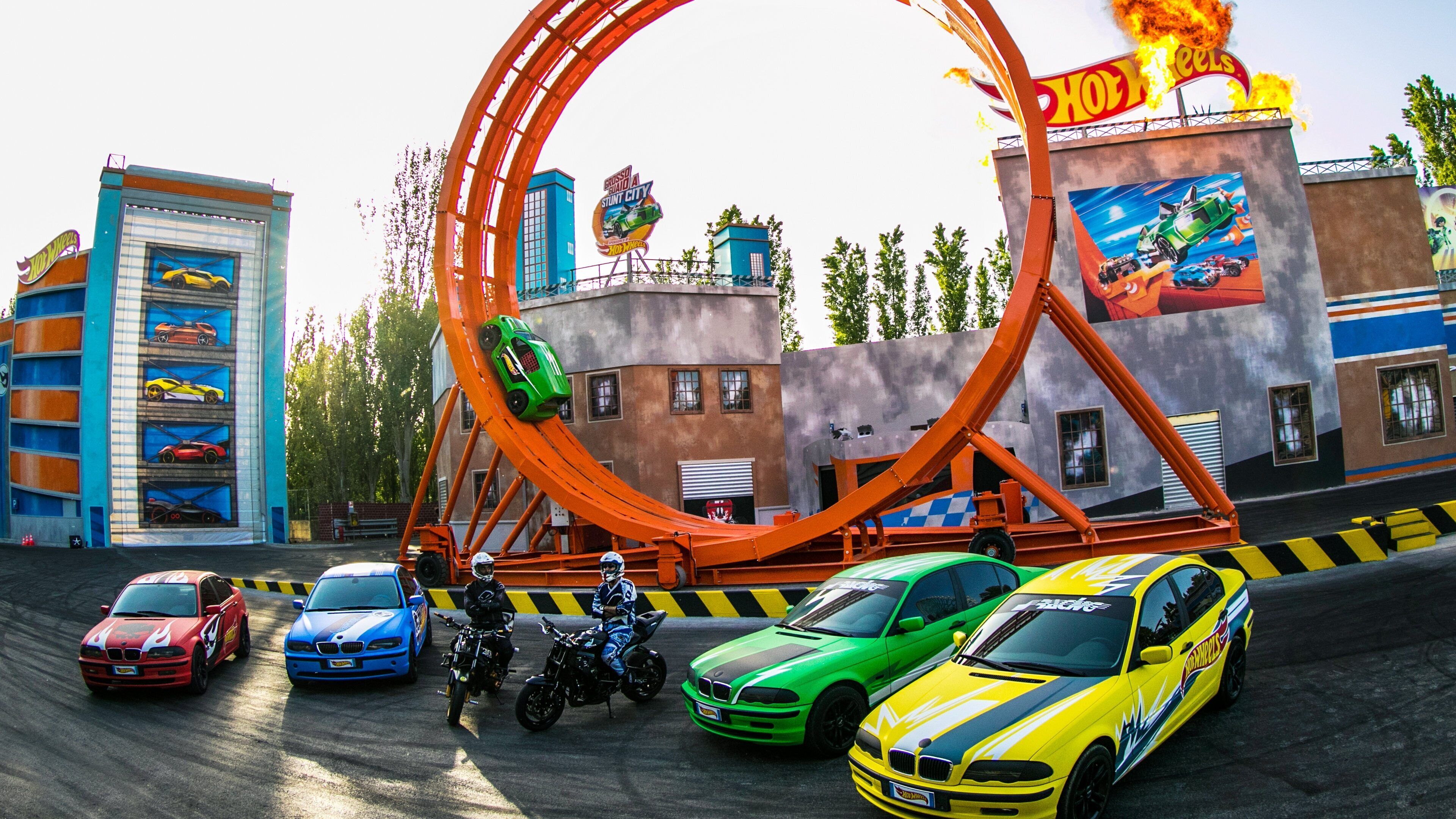 A roller coaster with cars and motorcycles, surrounded by buildings with car-themed murals.