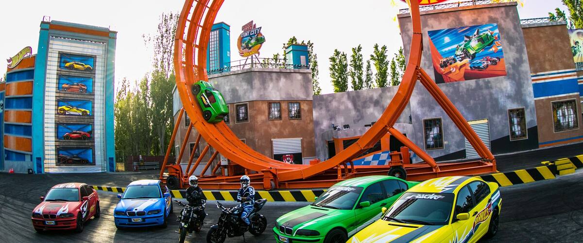 A roller coaster with cars and motorcycles, surrounded by buildings with car-themed murals.