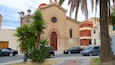 A church with a red door, palm trees, and parked cars.