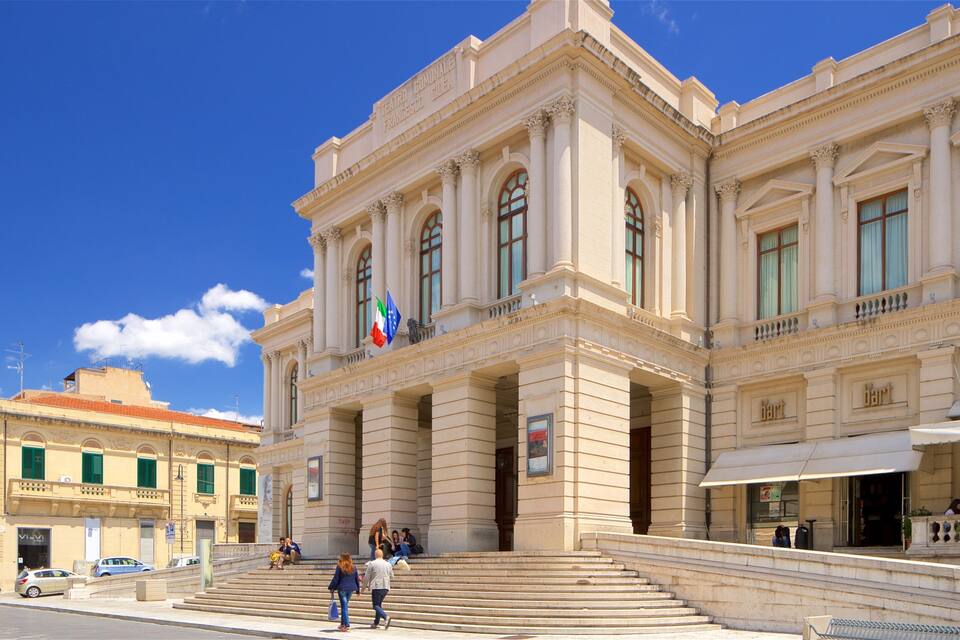 A grand neoclassical building with columns and arched windows, a flag, and a street with pedestrians.