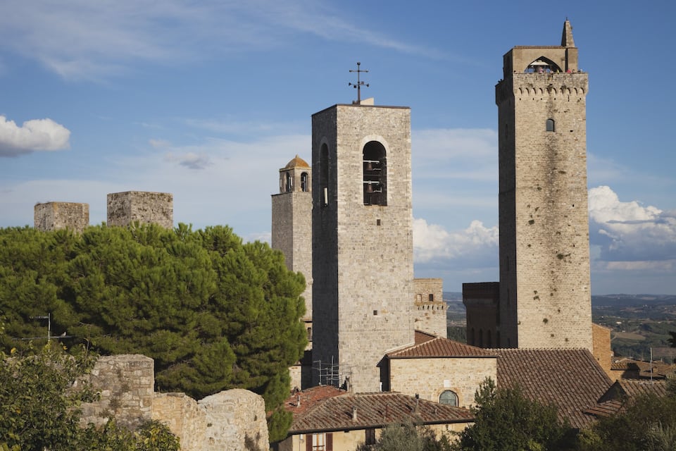 A historic stone church with two prominent towers, surrounded by ancient ruins and a dense forest.