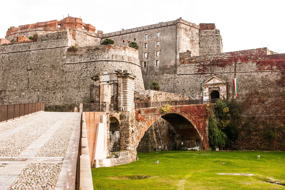 Una fortaleza de piedra histórica con un gran puente arqueado y un patio cubierto de césped.