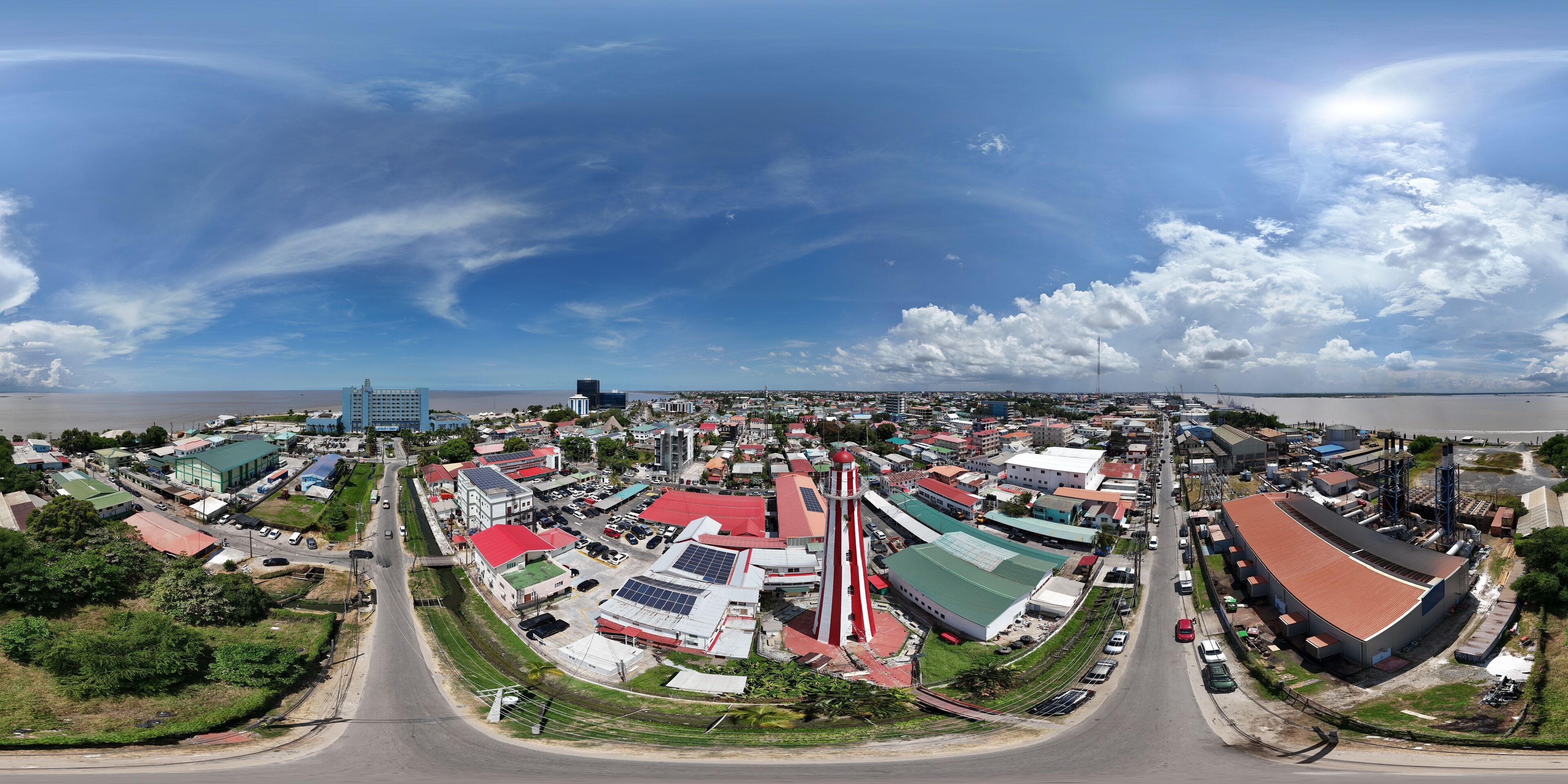 360 aerial photo taken with drone of red and white lighthouse in middle of neighborhood on sunny afternoon in Georgetown, Guyana