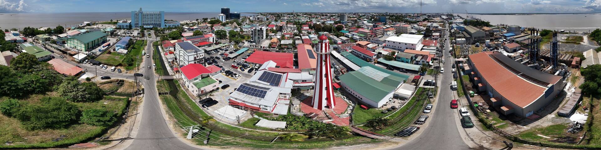 360 aerial photo taken with drone of red and white lighthouse in middle of neighborhood on sunny afternoon in Georgetown, Guyana