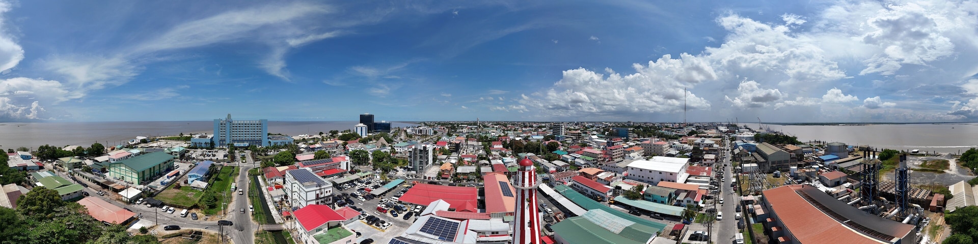 360 aerial photo taken with drone of red and white lighthouse in middle of neighborhood on sunny afternoon in Georgetown, Guyana
