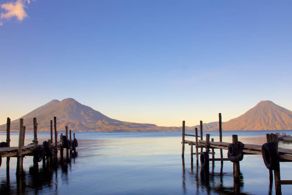 Un lago tranquilo con muelles de madera que se adentran en el agua, rodeado de montañas.