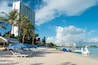 A beach with lounge chairs, umbrellas, palm trees, and a row of colorful boats.