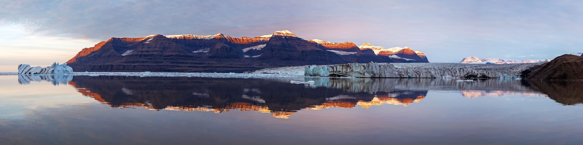 A panorama of Vikinge Bay, Scoresby Sund, Greenland, showing icebergs, mountains, a glacier, and polar bears on the moraine to the right.