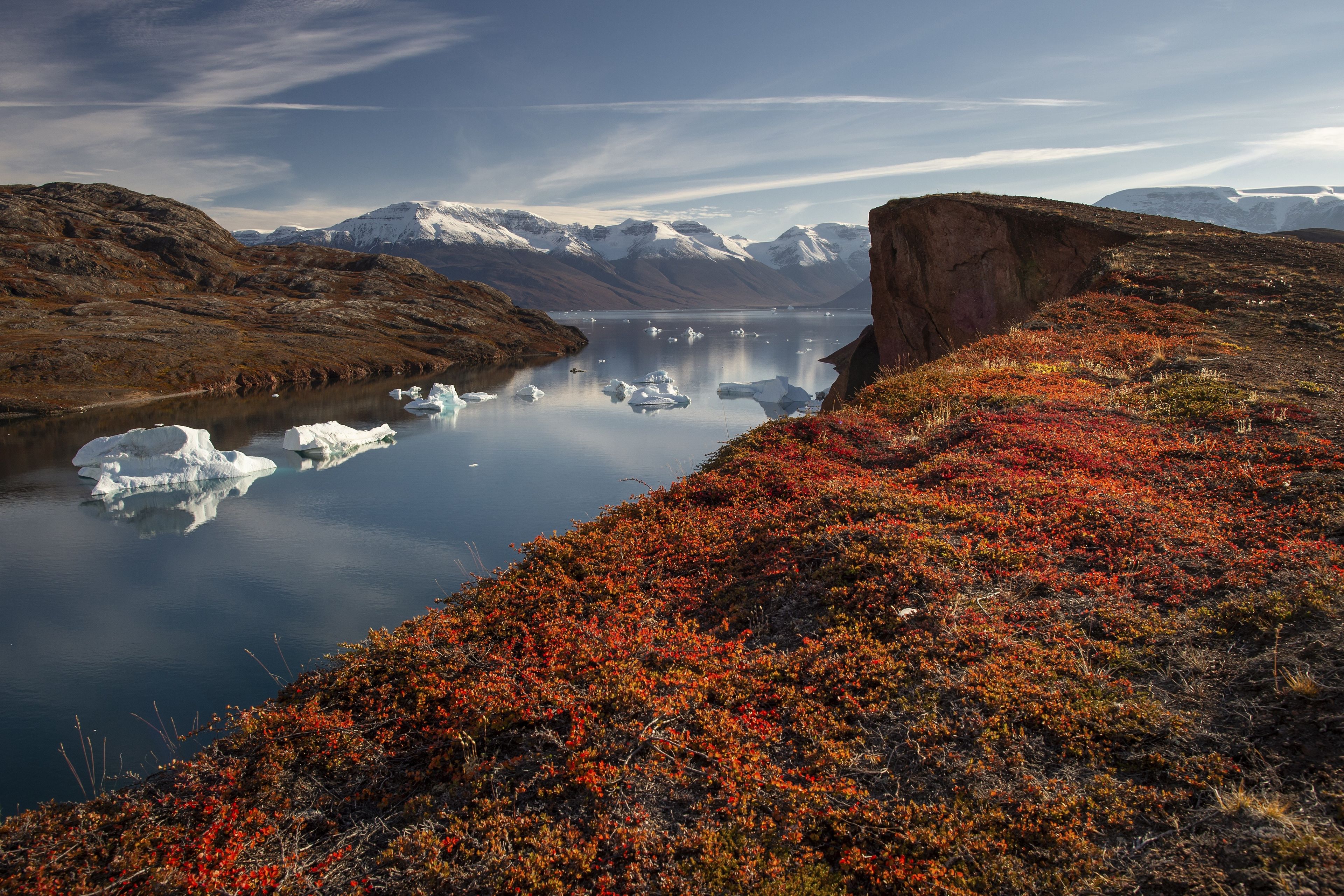 A glacier with icebergs, a river, and a mountainous landscape.