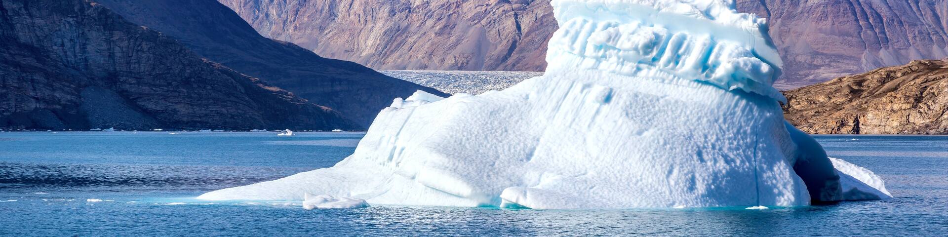 A large iceberg in a fjord with mountains in the background.