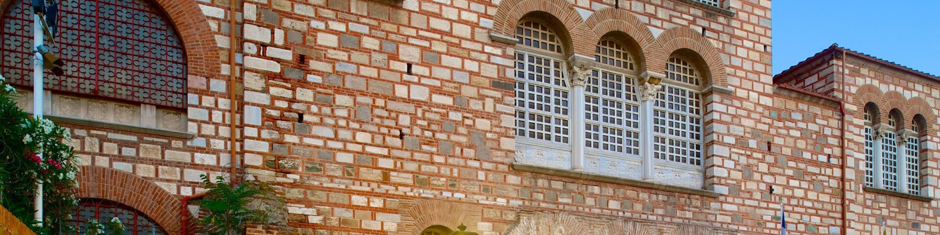Um edifício histórico com paredes de tijolos vermelhos, janelas em arco e uma escadaria de pedra.
