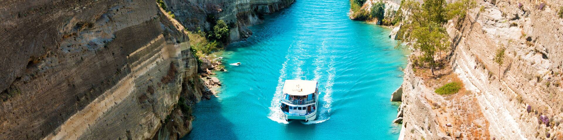 Beautiful scenery of the Corinth Canal in a bright sunny day against a blue sky with white clouds. Among the rocks floating white ship in turquoise water.
