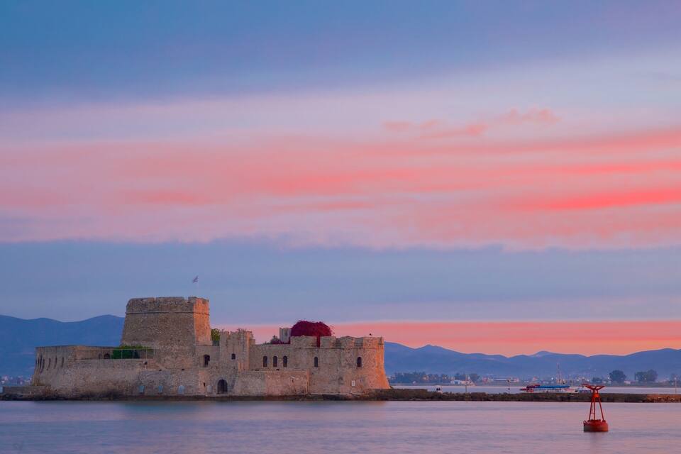 Un château de pierre historique, situé sur une petite île, entouré d’eaux calmes et avec des montagnes en toile de fond.