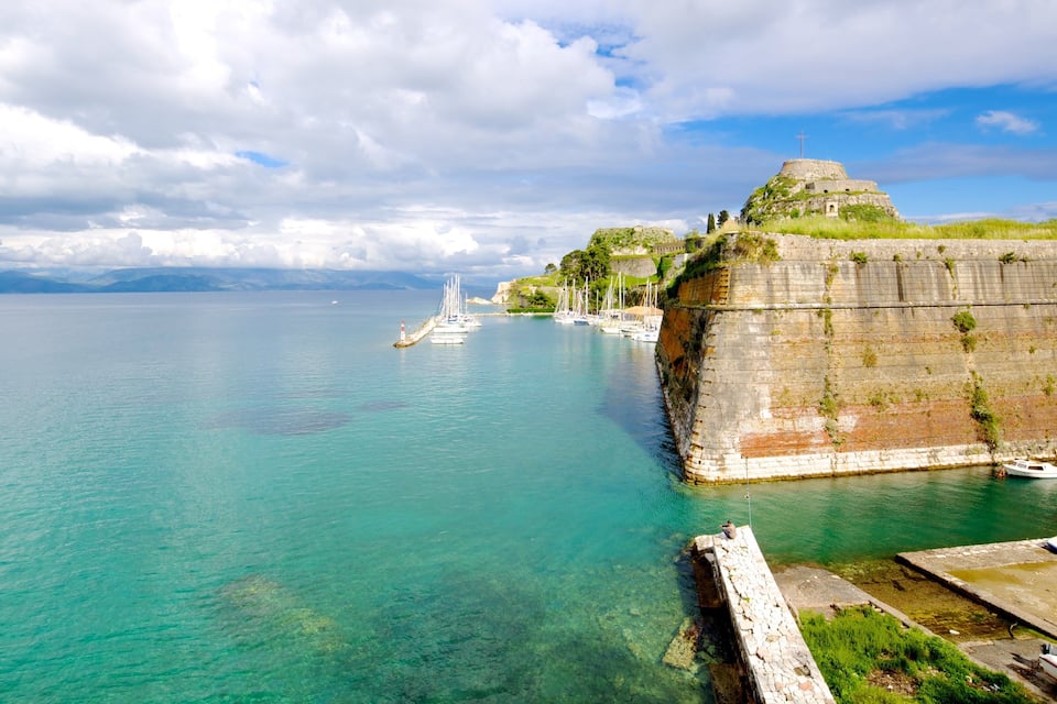 Une fortification côtière dotée d’un phare, des eaux turquoise cristallines et des bateaux amarrés à proximité.