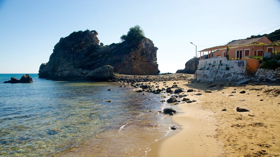 A rocky coastline with clear waters, a large rock formation, and a building with a sign reading "Cafe Bar".