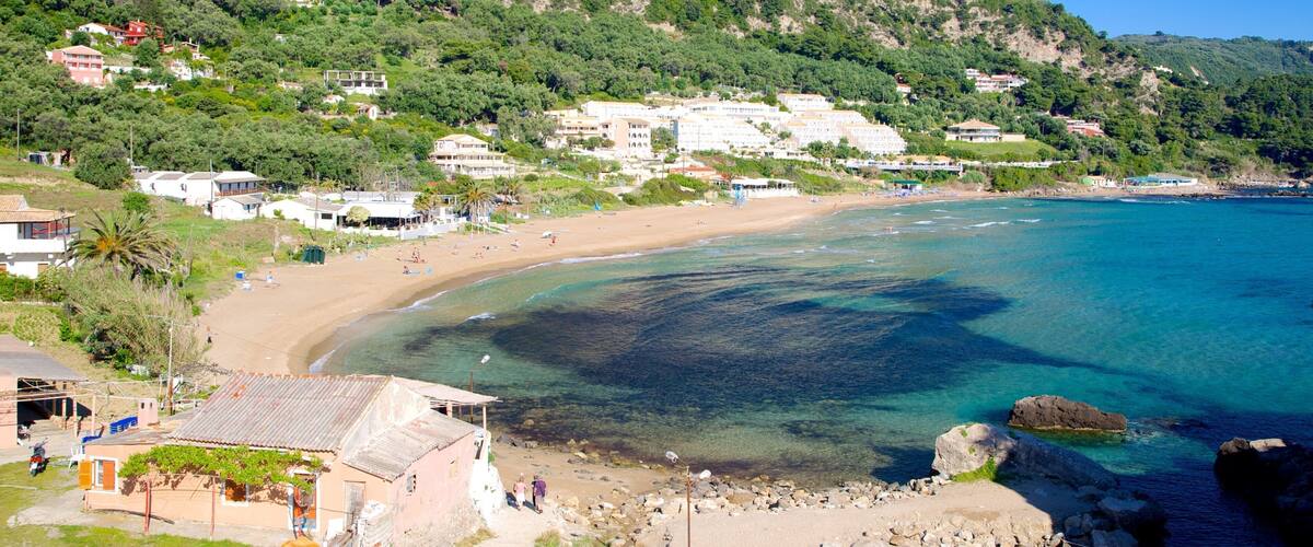 A coastal town with a sandy beach, clear blue waters, and lush green hills in the background.