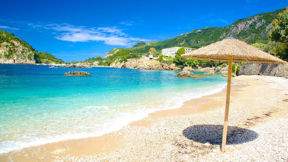A beach with clear turquoise water, a thatched umbrella, and rocky cliffs.