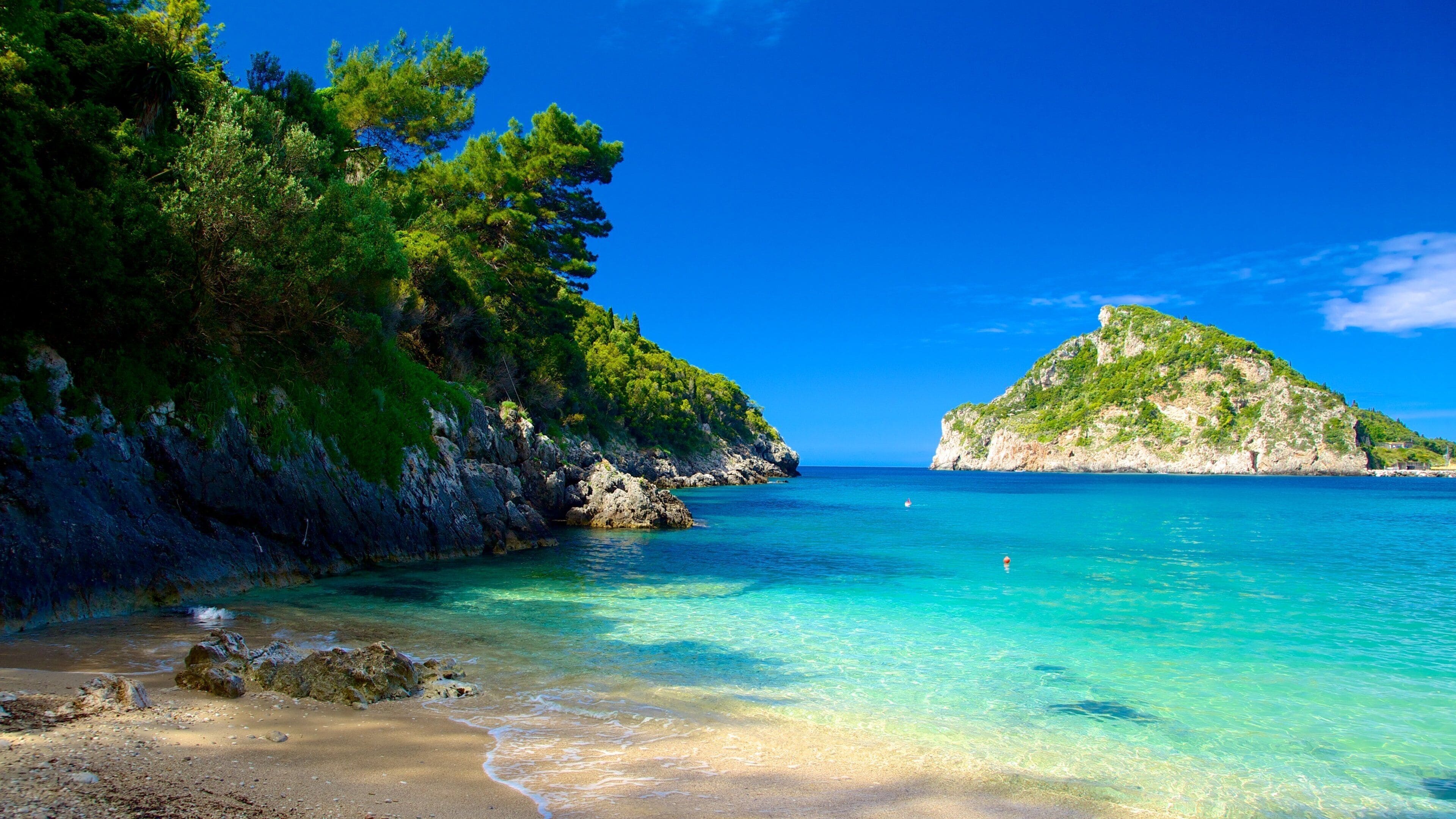A clear turquoise sea, rocky coastline, and lush green hills.