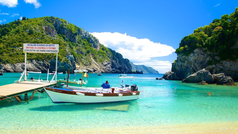 A boat docked at a turquoise harbor surrounded by rocky cliffs and lush greenery.