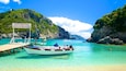 A boat docked at a turquoise harbor surrounded by rocky cliffs and lush greenery.