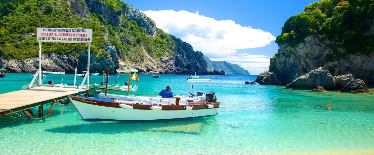 A boat docked at a turquoise harbor surrounded by rocky cliffs and lush greenery.
