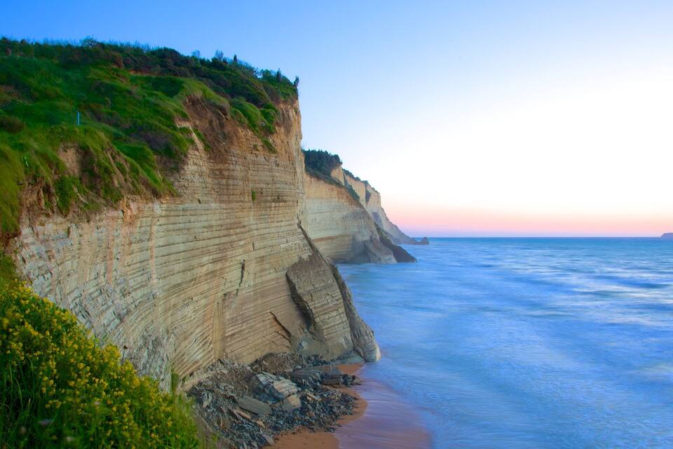 Une falaise côtière aux formations rocheuses stratifiées, avec une plage au coucher du soleil.