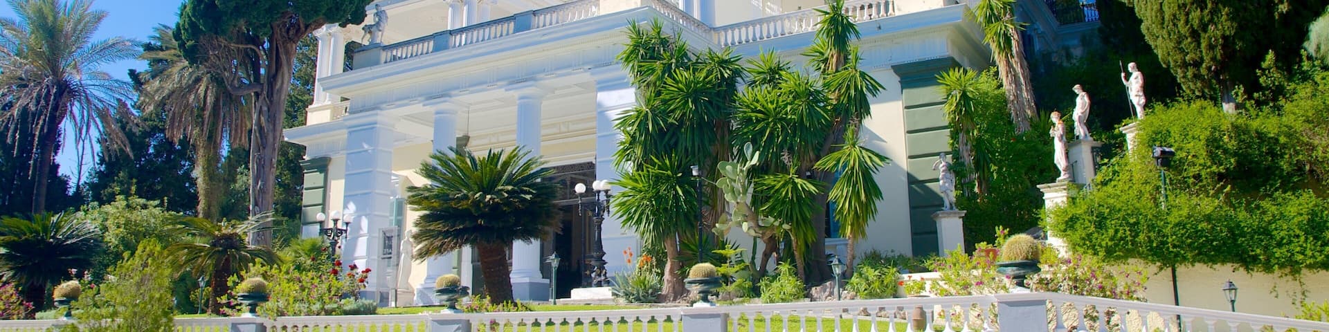 A classical building with columns, statues, and a white fence.