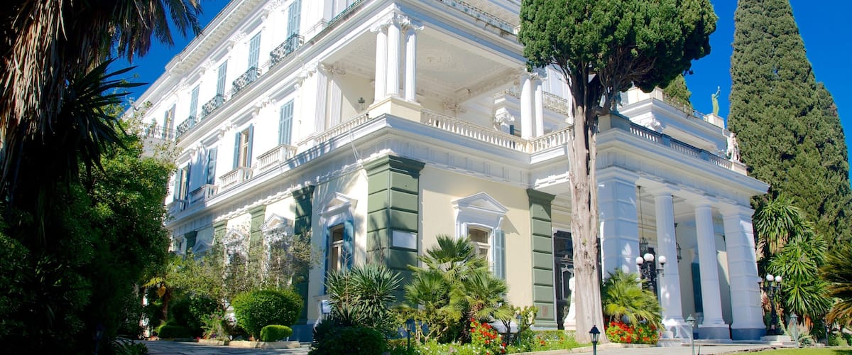 A classical building with columns and statues, surrounded by lush greenery and a clear blue sky.