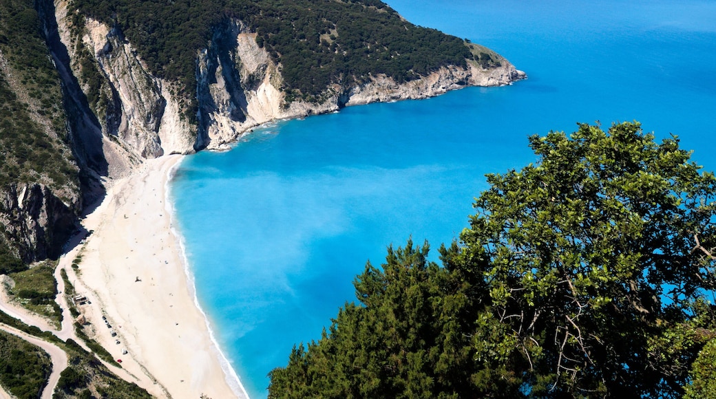 Aerial scene of Myrtos Beach in bright morning light, featuring turquoise sea and lush green coast.