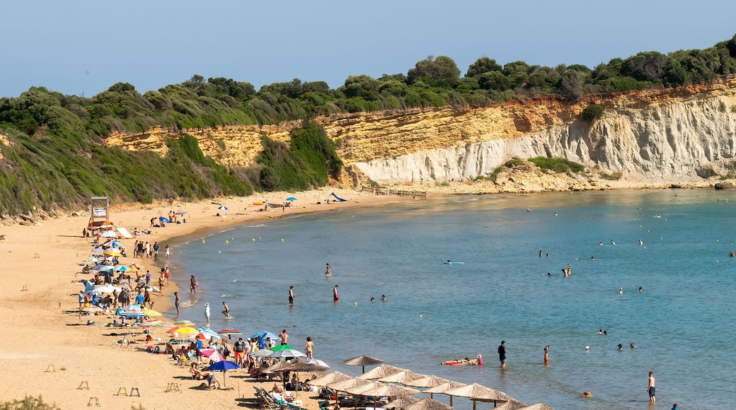 Une plage côtière aux eaux bleues et limpides, avec un rivage sablonneux et une falaise rocheuse couverte de végétation.