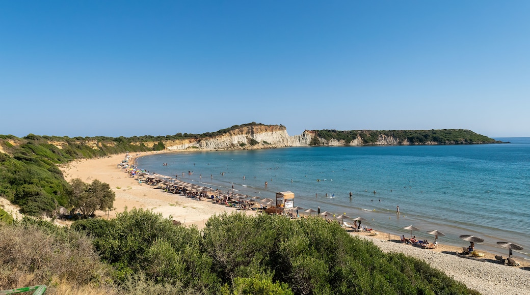 Une plage côtière aux eaux d’un bleu limpide, bordée de sable fin, avec une falaise imposante en arrière-plan.
