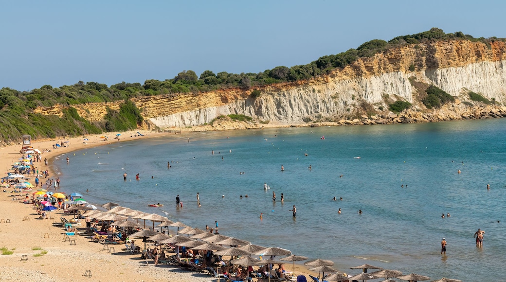 Une plage avec une eau d’un bleu limpide, des gens qui se baignent et prennent des bains de soleil, et des falaises en arrière-plan.
