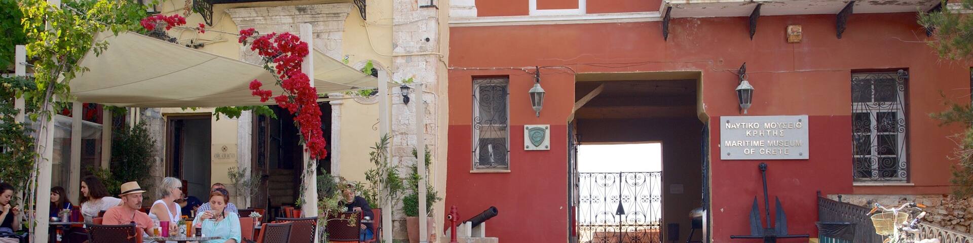 Una calle empedrada con mesas al aire libre, un hidrante rojo y el cartel de un museo marítimo.