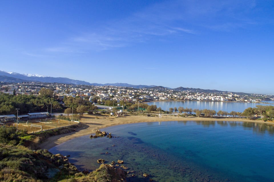 A coastal town with a clear blue lake, sandy beach, and mountains in the background.