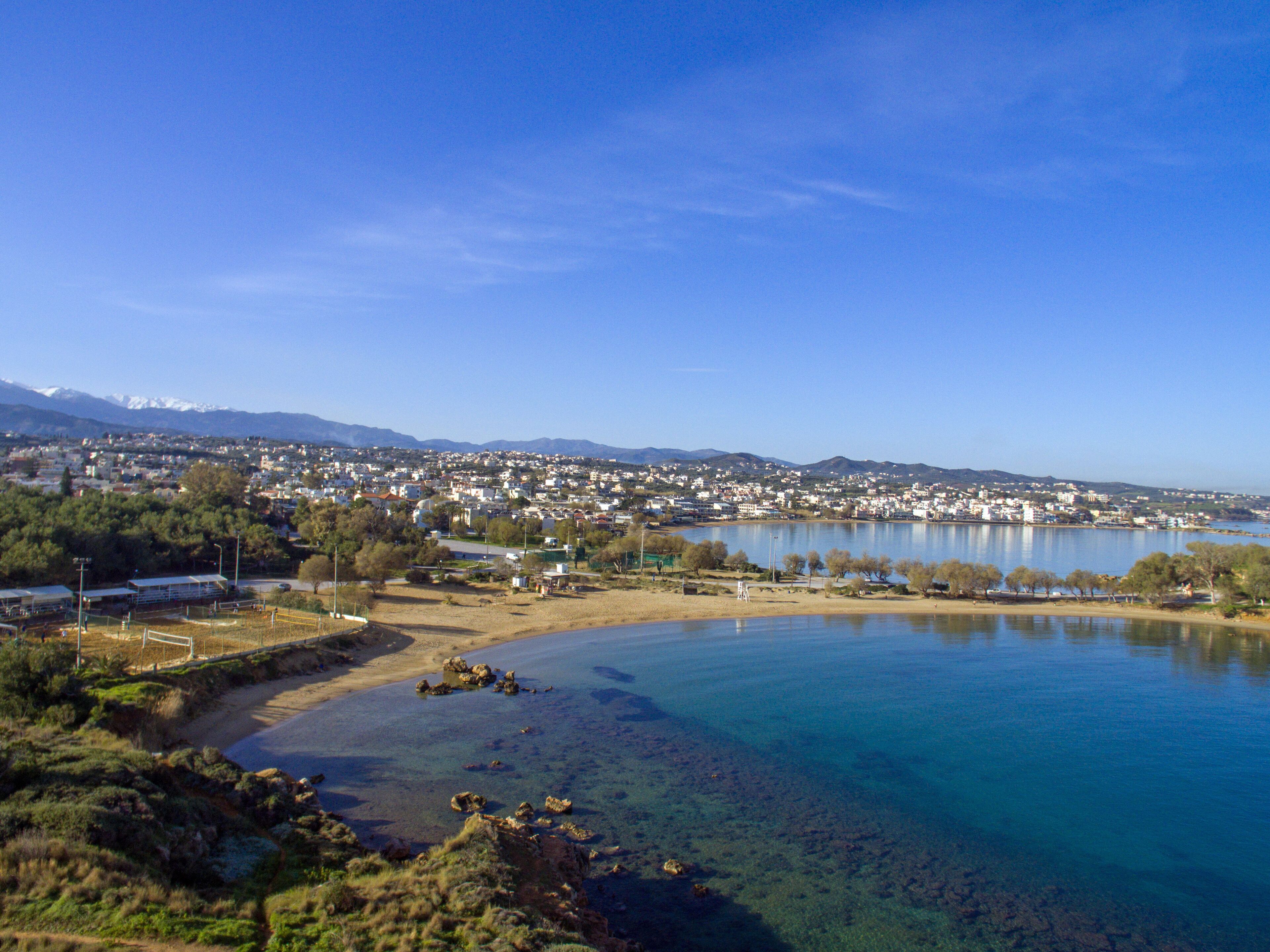 A coastal town with a clear blue lake, sandy beach, and mountains in the background.