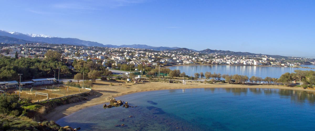 A coastal town with a clear blue lake, sandy beach, and mountains in the background.
