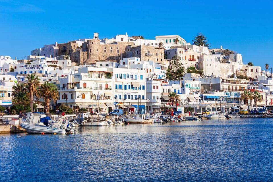 A coastal town with white buildings, a harbor with boats, and palm trees.